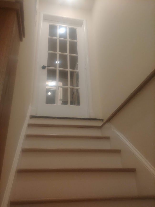 Staircase leading up to a white door with glass panes. Beige walls, wooden steps and handrail.