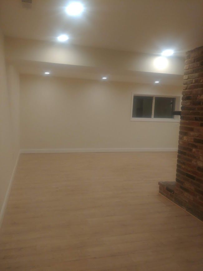 Empty room with light-colored flooring, beige walls, recessed ceiling lights, and brick fireplace.