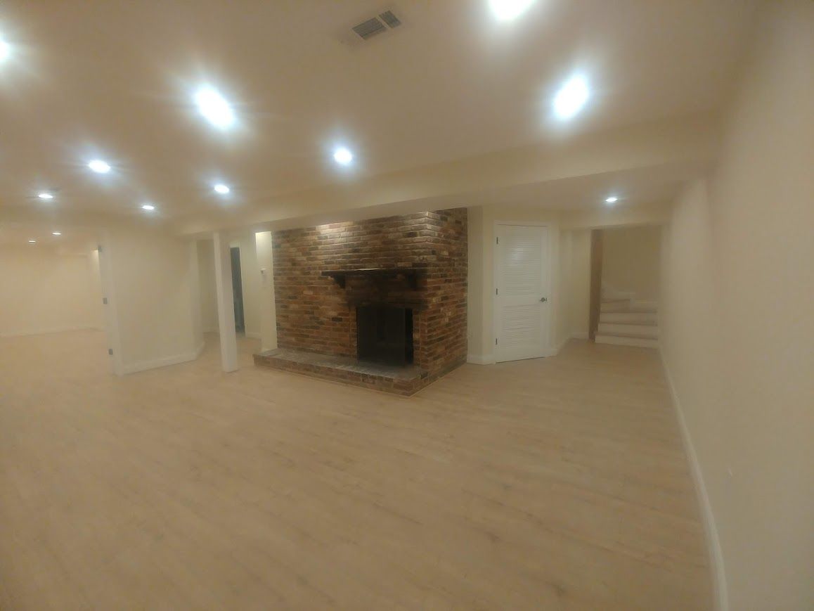 Basement interior with fireplace, light wood flooring, and recessed lighting.
