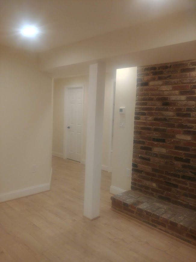 Interior view of a room with brick fireplace, white support column, and light-colored wood floors.