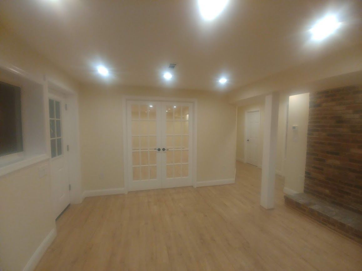Empty, bright basement with light wood floor, French doors, and stone fireplace.
