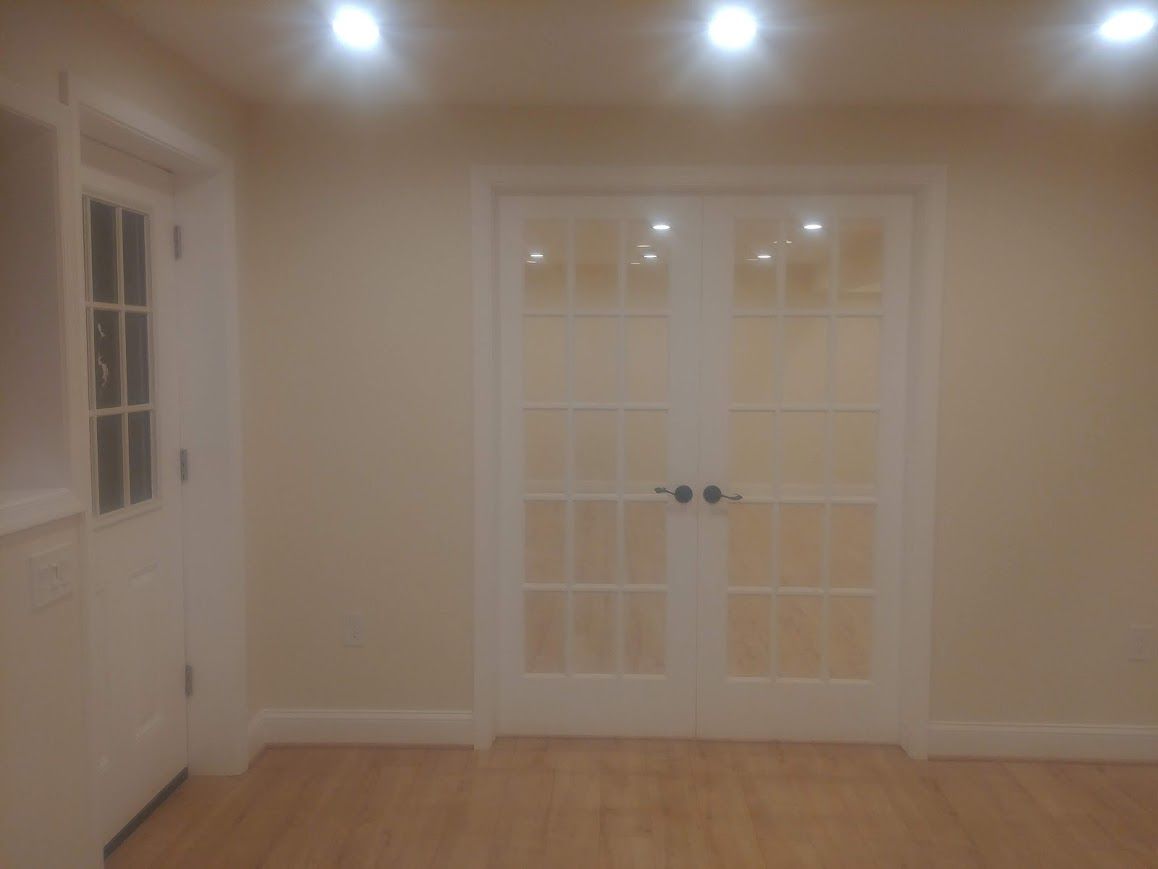 White French doors and a door with paneled glass in a room with light-colored walls and wood flooring.