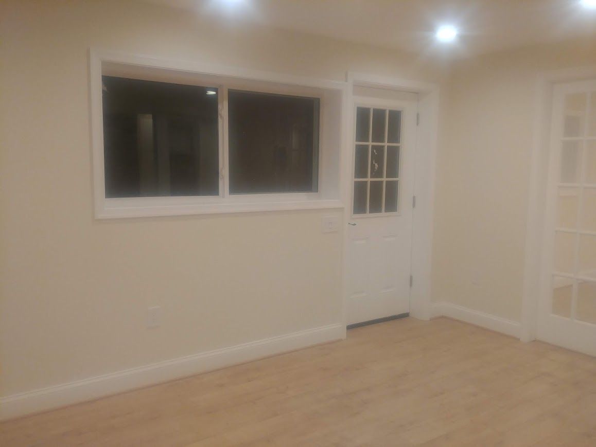 Empty room with window, door, and wood floor. Beige walls, white trim.