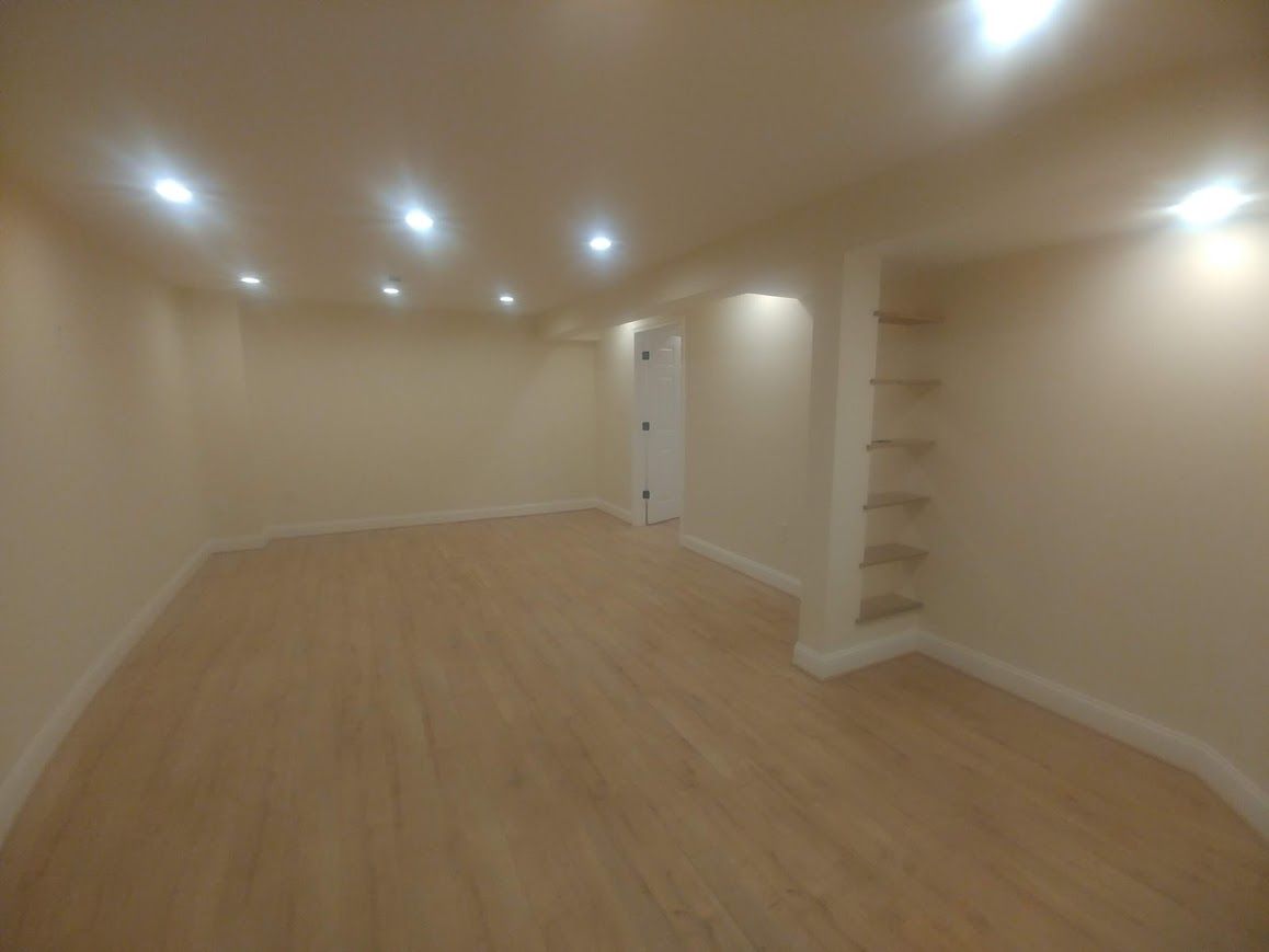 Empty room with light wood floors, beige walls, recessed lighting, and built-in shelves.