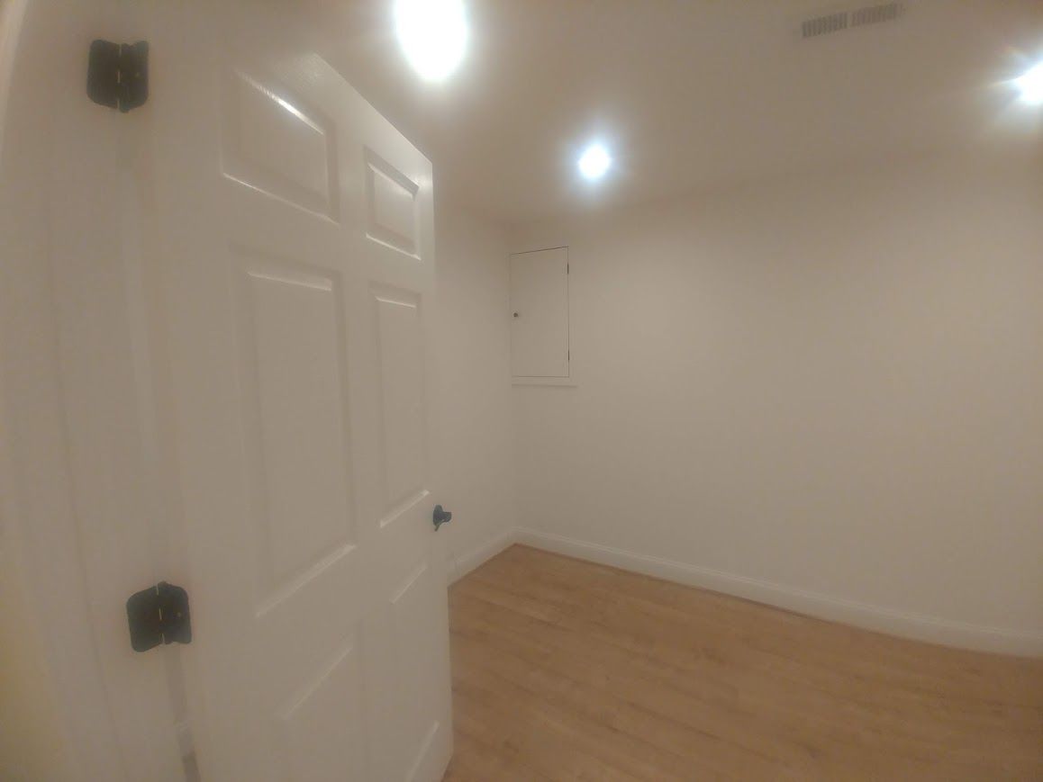 White door slightly ajar leading into a small room with light wood floors and white walls.