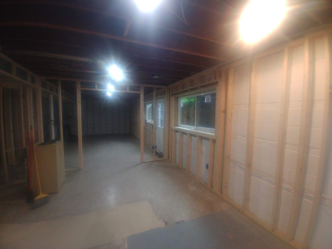 Basement interior under construction with exposed wooden framing, concrete floor, and overhead lighting.
