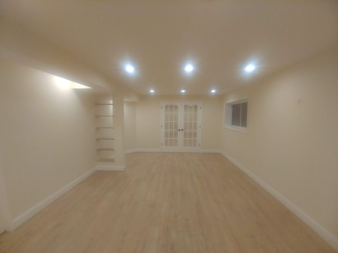 Empty, well-lit room with light wood floors, recessed ceiling lights, and double glass doors.