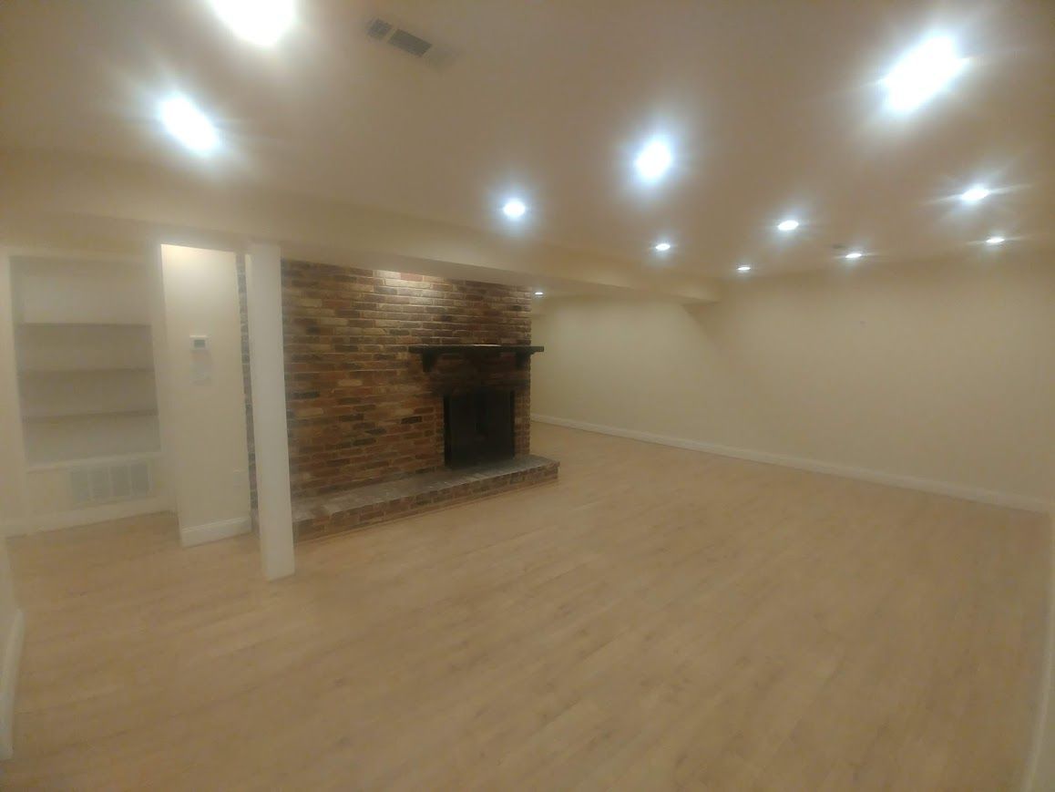 Empty room with brick fireplace, light wooden floor, and recessed lighting.
