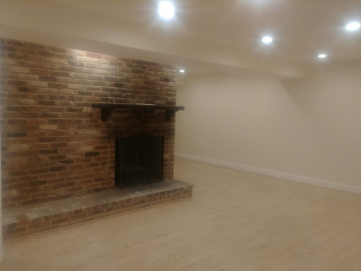 Brick fireplace in an empty room, beige walls and floor, recessed lights overhead.