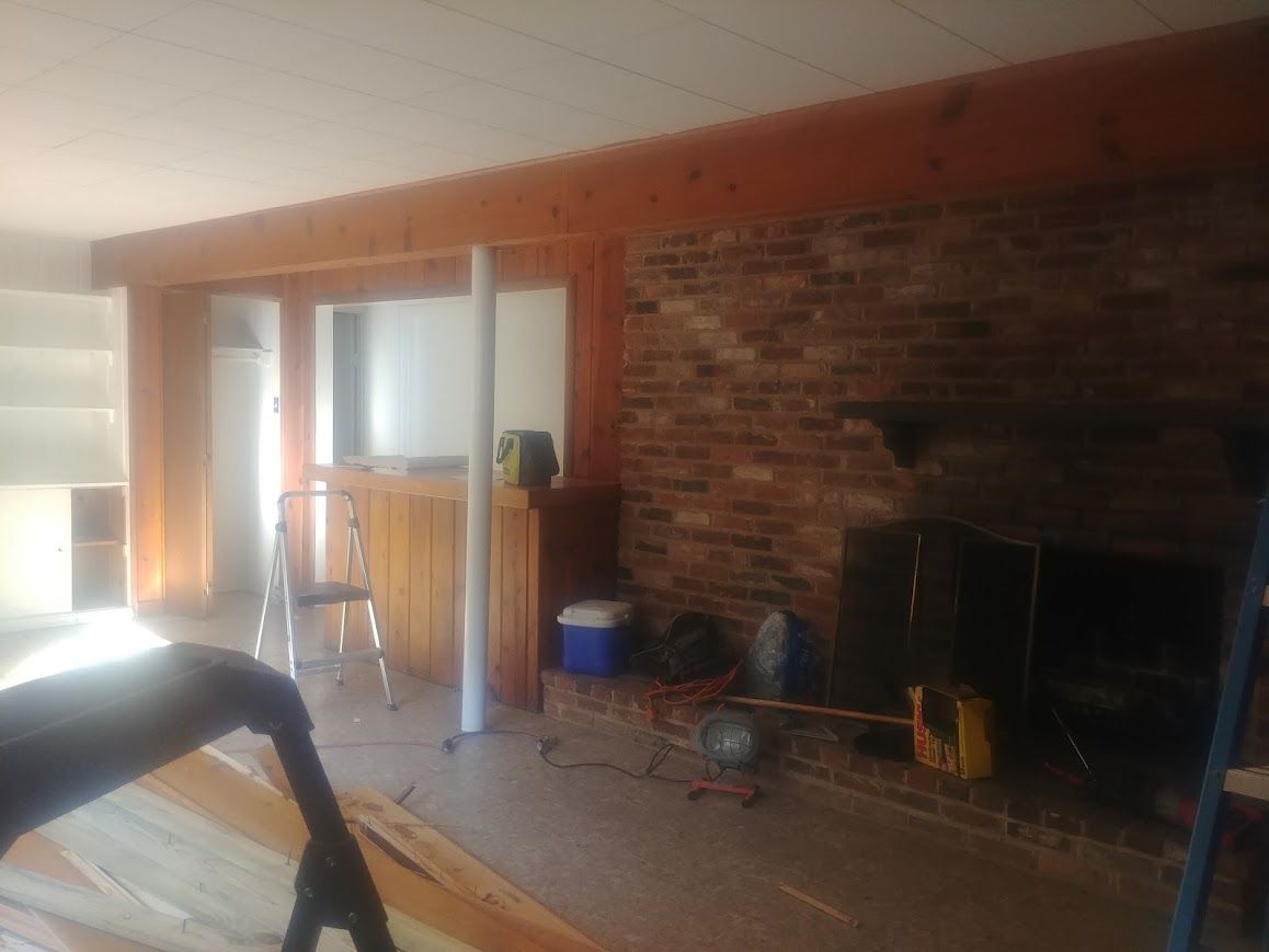 Interior room renovation in progress; brick fireplace, wooden beams, support poles.