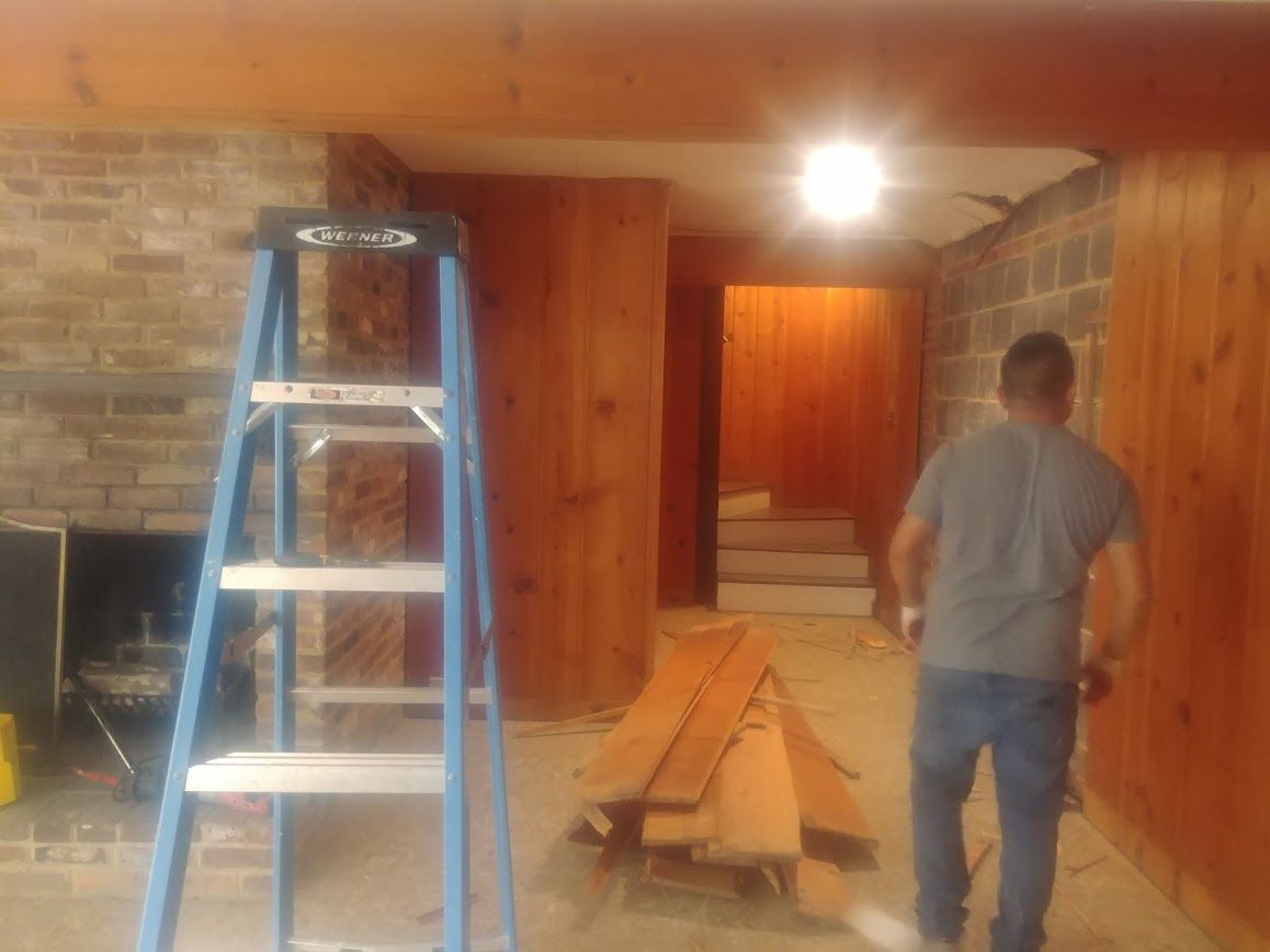 A person inside a room with wood paneling, a fireplace, and a ladder; construction in progress.