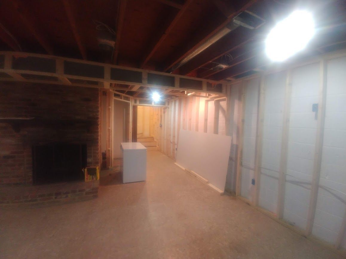 Basement under construction, with wooden framing, exposed beams, and a fireplace. Drywall is partially installed.