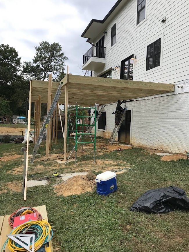 Construction of a wooden deck attached to a two-story white house; tools and ladders are present.
