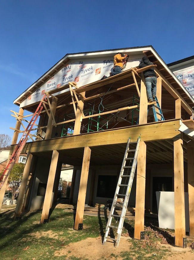 Construction workers building a wood deck on a house, with ladders and blue sky.