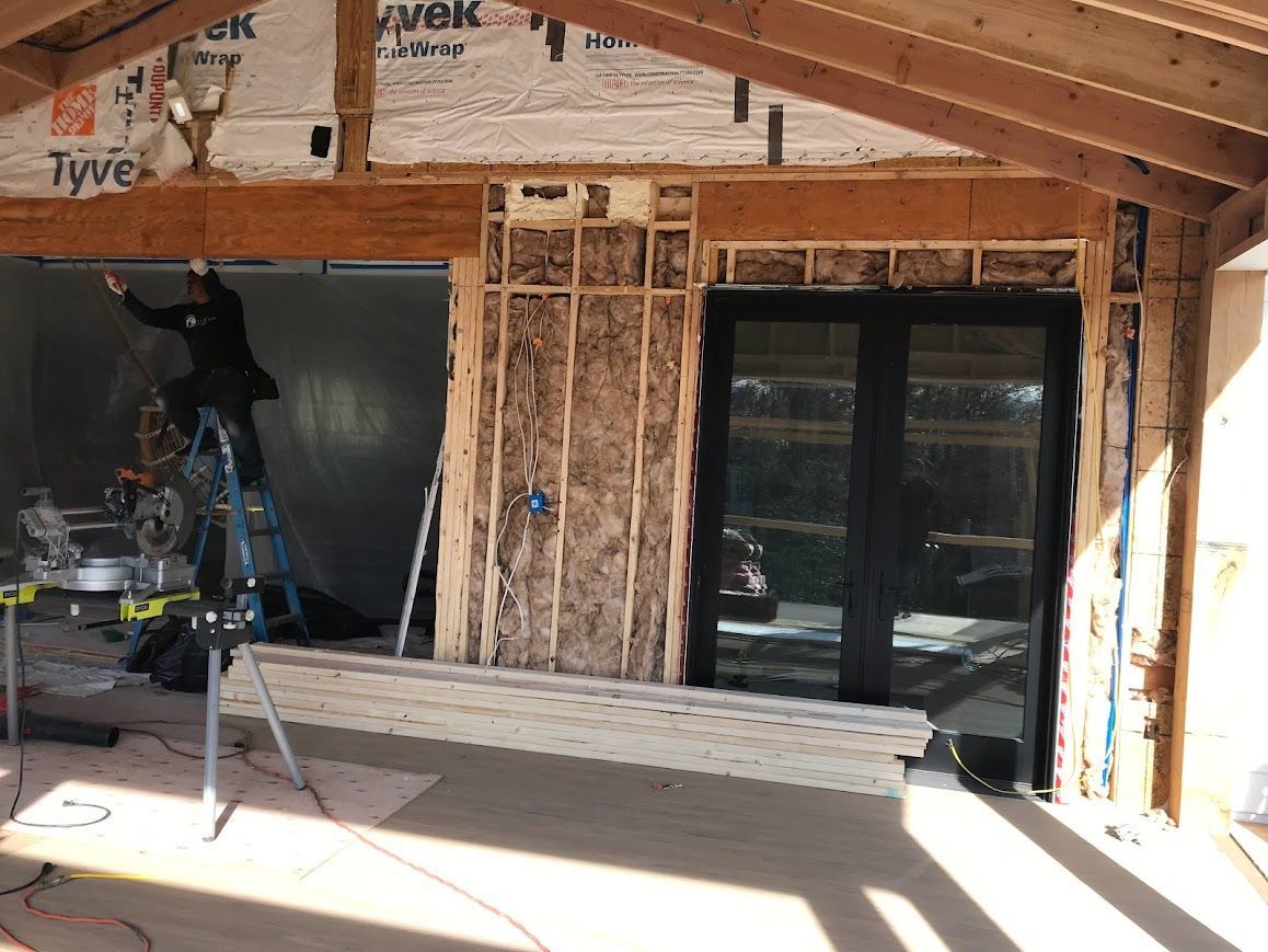 Construction site with partially built wooden frame. Person on ladder working on the structure near an opening.