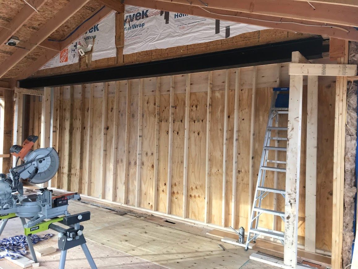 Interior view of a wooden framed wall under construction. Saw and ladder present.