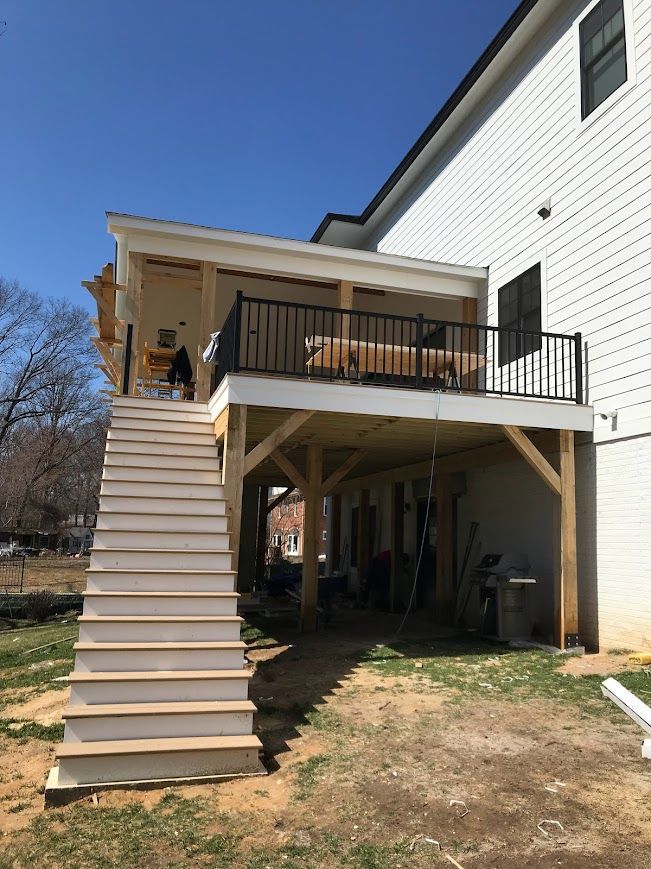 A two-story deck attached to a white house with stairs leading down to a yard on a sunny day.