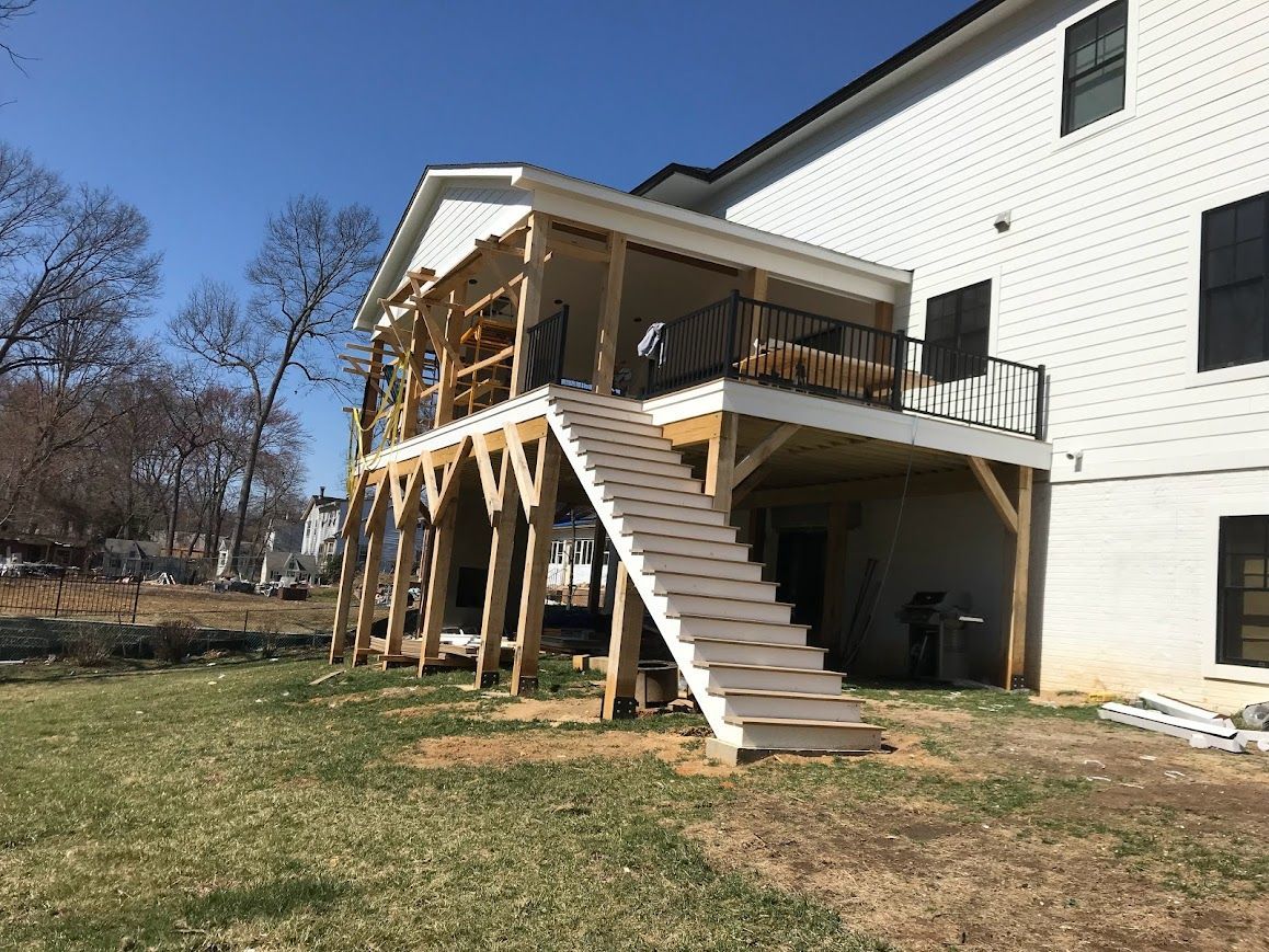 Multi-level wooden deck with stairs attached to a white building; clear blue sky.