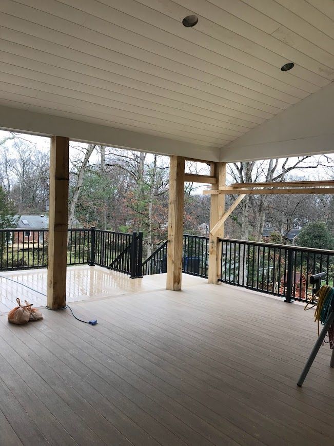 Covered outdoor deck under construction, composite decking, black railing, light wood posts, tan ceiling.