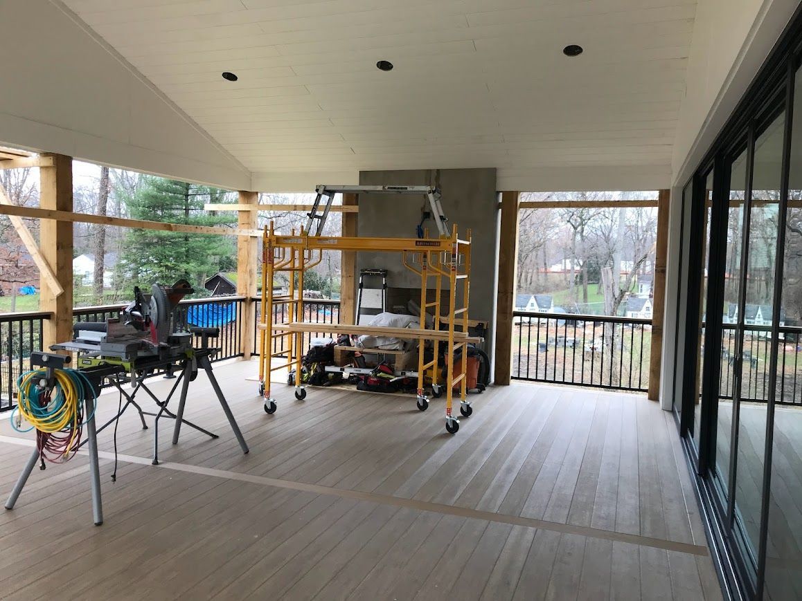 Deck under construction with tools, scaffolding, and partially installed railing, overlooking a wooded area.