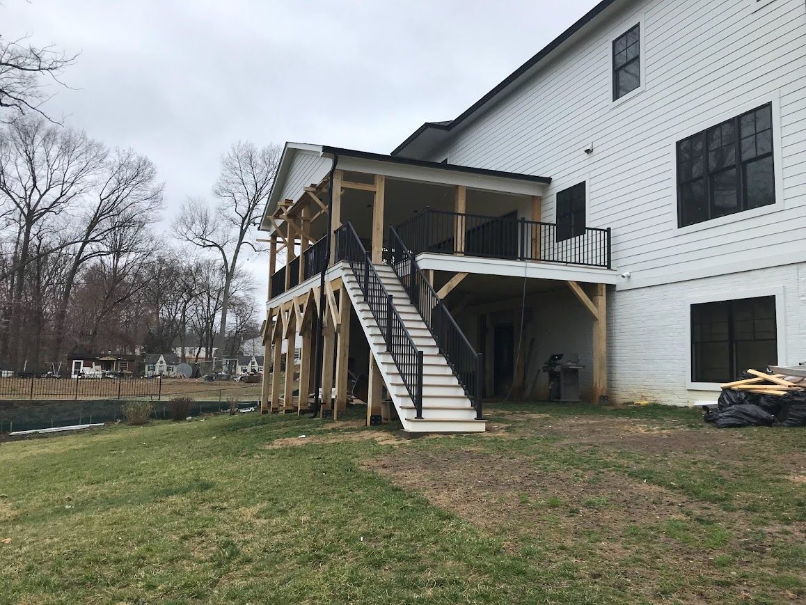 A two-story screened porch with stairs attached to a white building. Construction in progress, cloudy day.