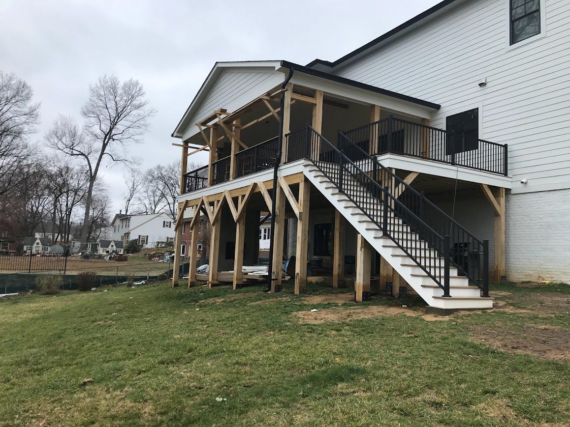Two-story wooden deck with stairs attached to a white brick house, viewed from the backyard.