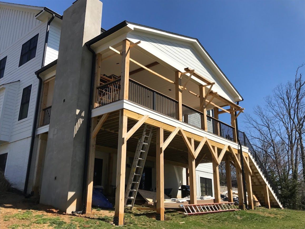 Construction of a two-story wooden deck attached to a white house with a chimney; blue sky.
