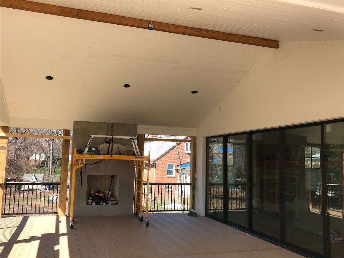 Outdoor covered patio under construction with fireplace, wood beam, and glass doors.