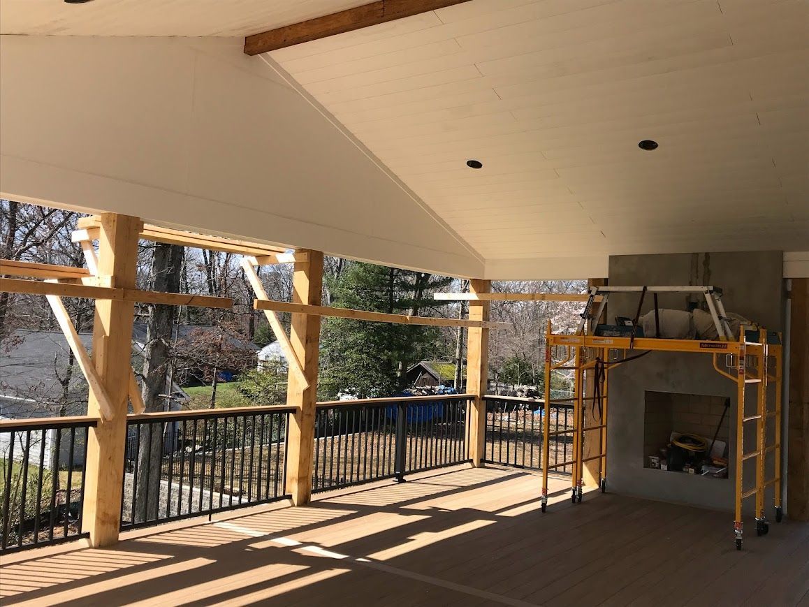 Covered outdoor deck with wooden posts, black railing, fireplace, and scaffolding.