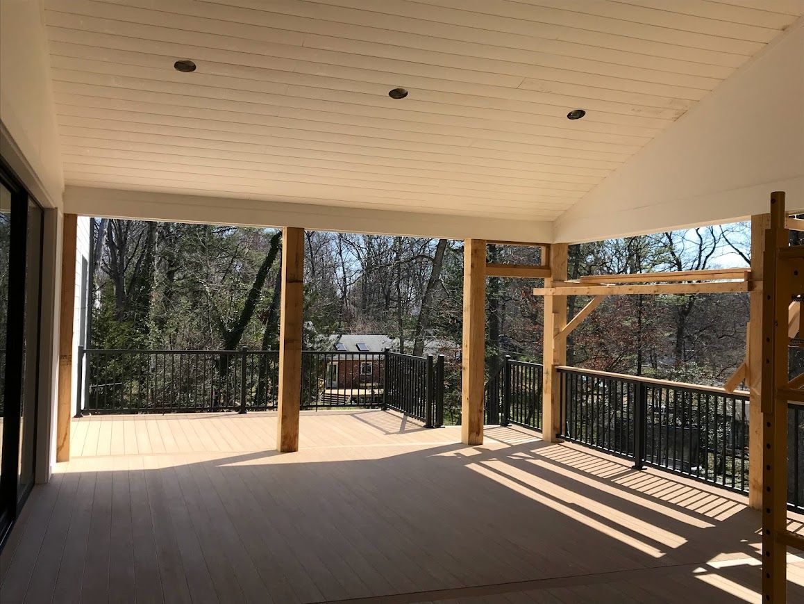 Spacious outdoor deck with brown planks, black railing, and wooden support beams, overlooking trees.