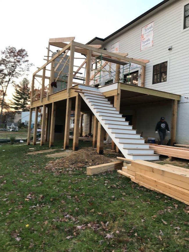 Deck construction in progress; wooden frame with stairs leading to elevated platform. A person walks below the deck.
