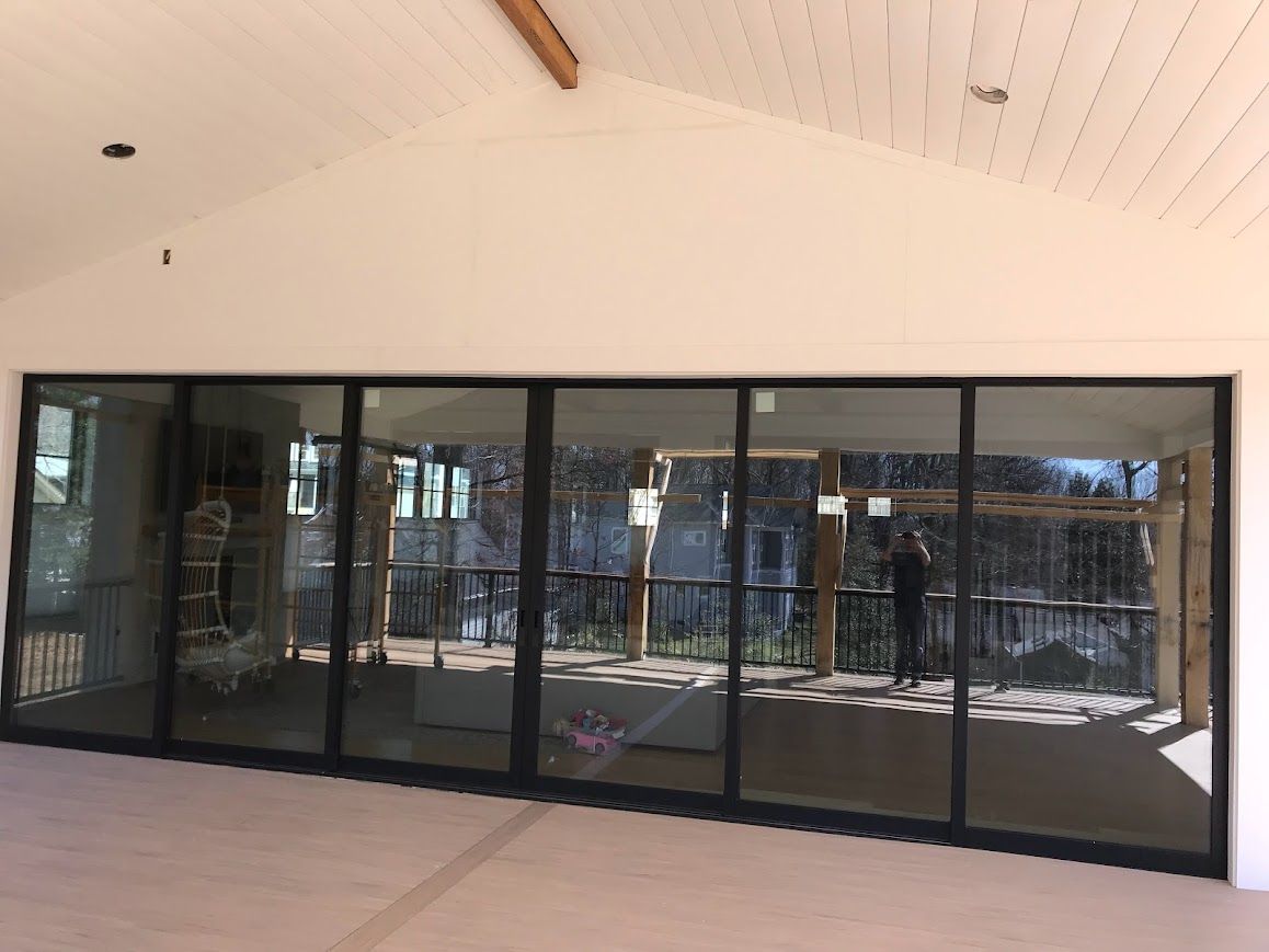 Large glass doors in a white-walled room, reflecting a porch with a person standing on it.