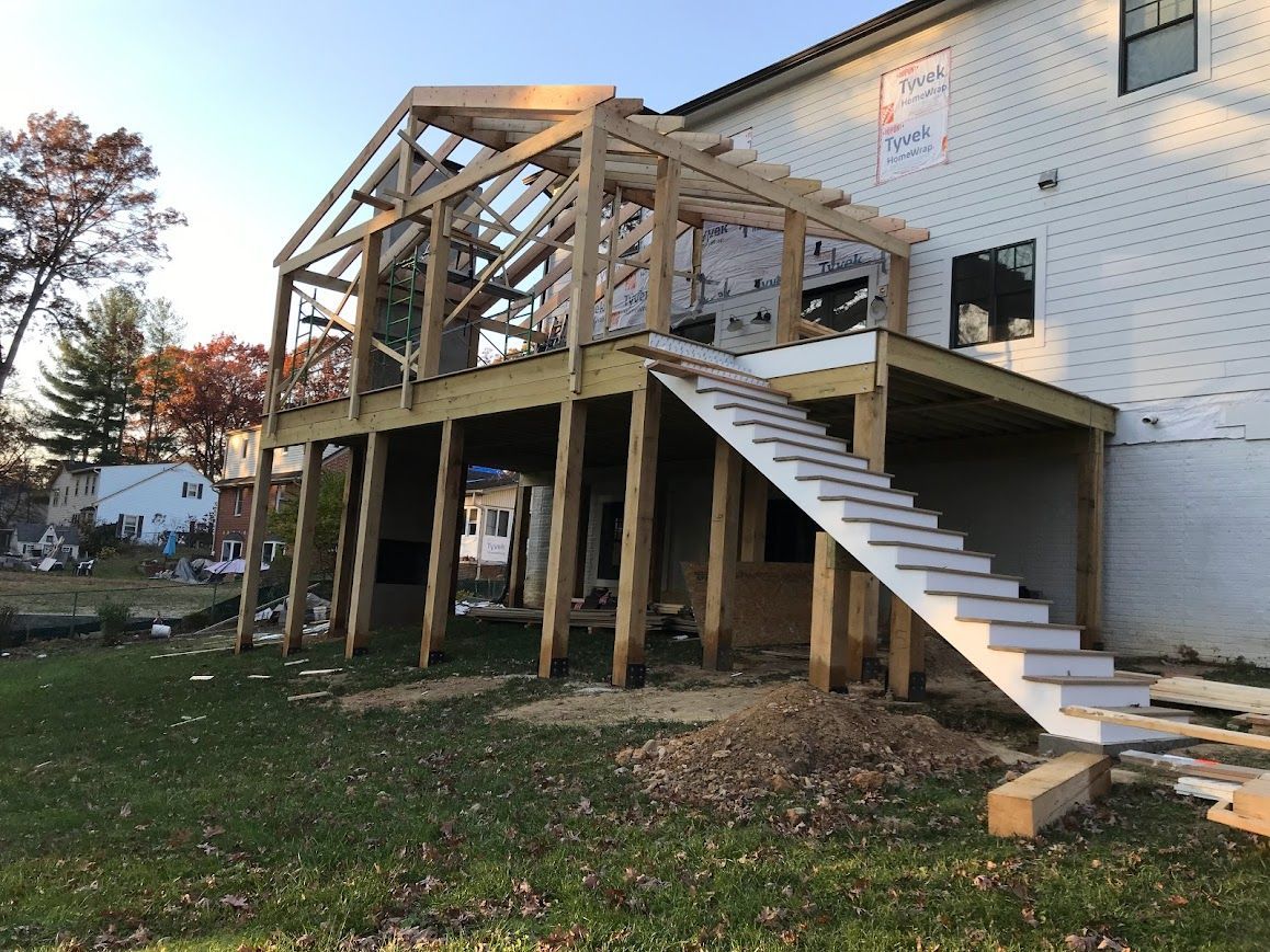 Wooden deck under construction attached to a white brick house, with stairs.