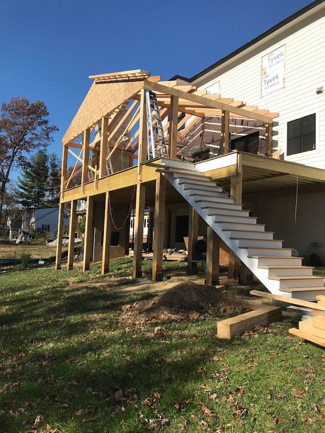Wooden deck under construction with stairs and roof frame attached to a house.