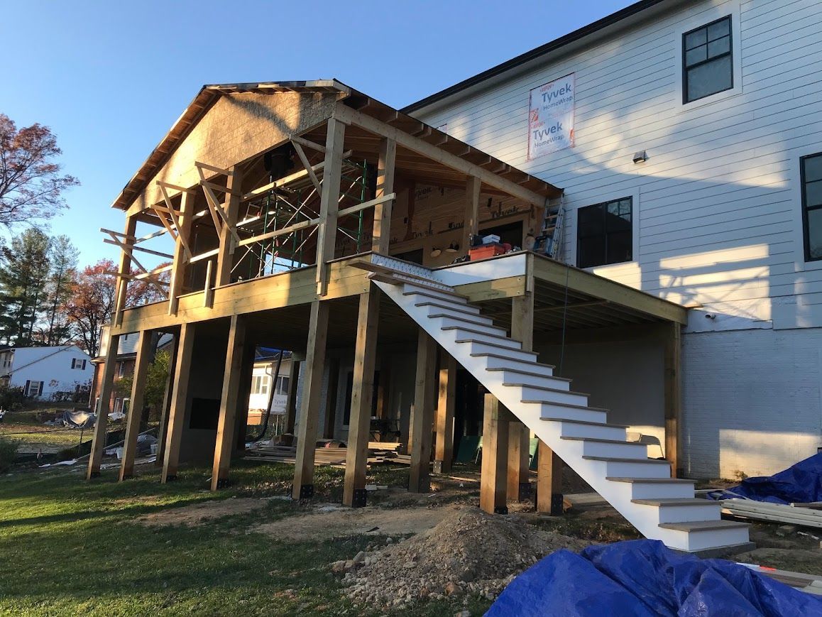 Construction of a wooden deck with stairs and a covered porch attached to a two-story house.