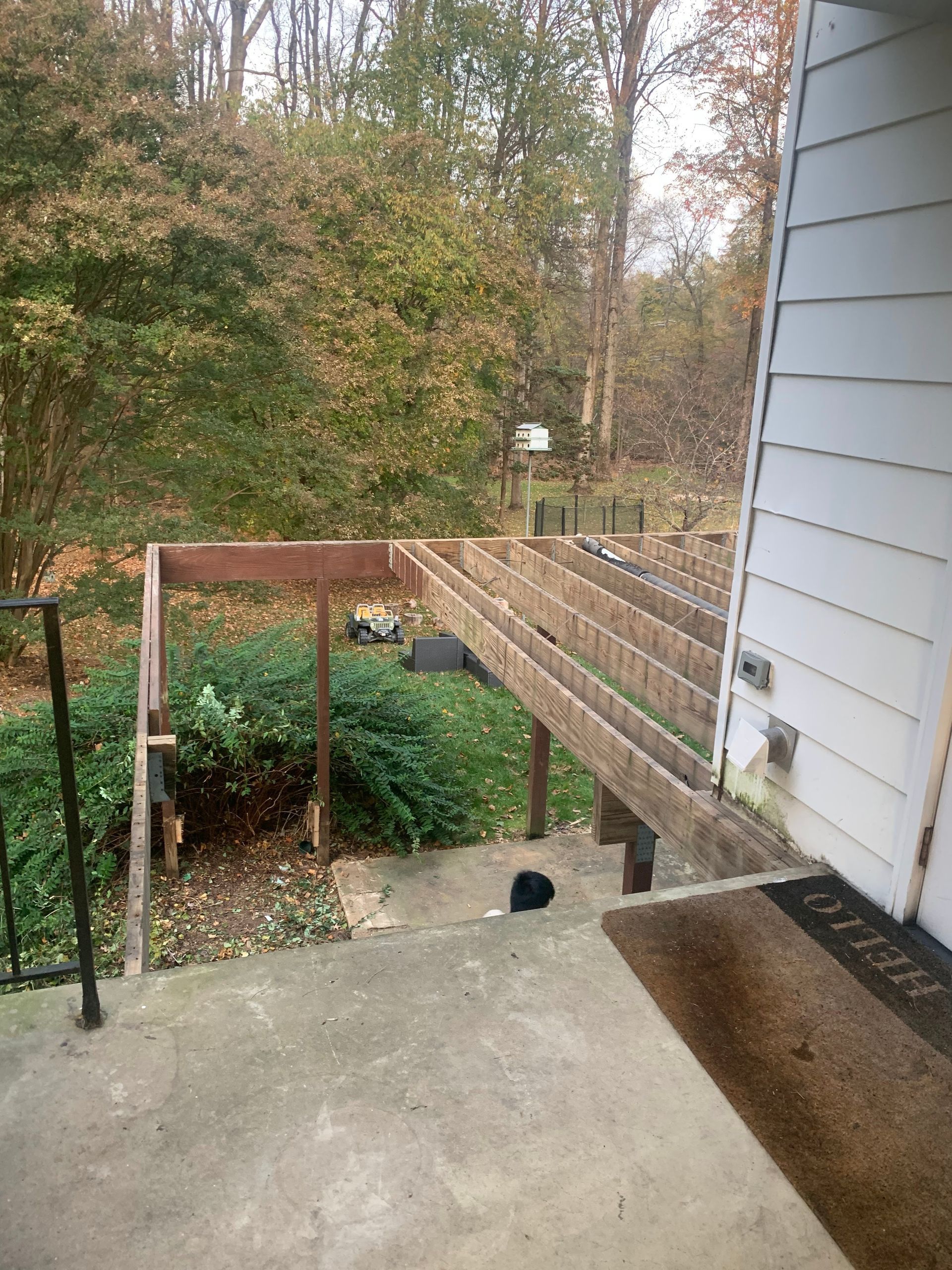 Partially built wooden deck with a concrete landing next to a house with a wooded background.