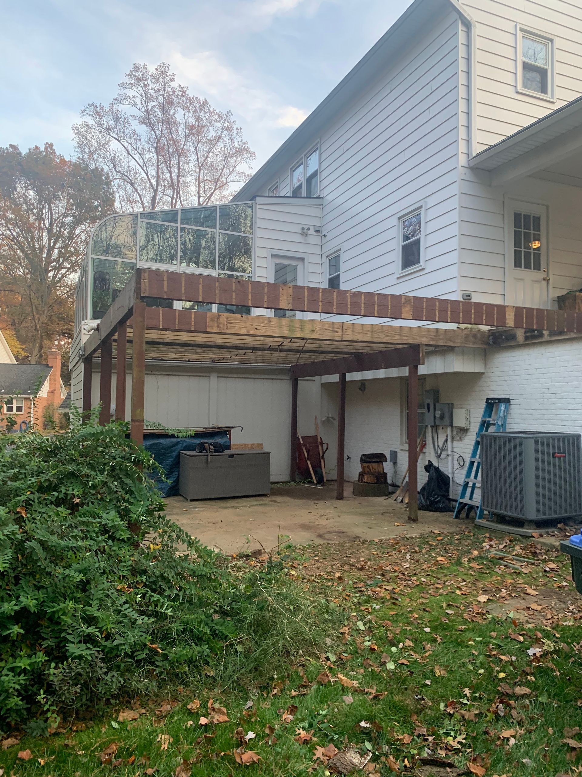Backyard with a two-story house, a pergola, and ground-level patio with shrubs and lawn.