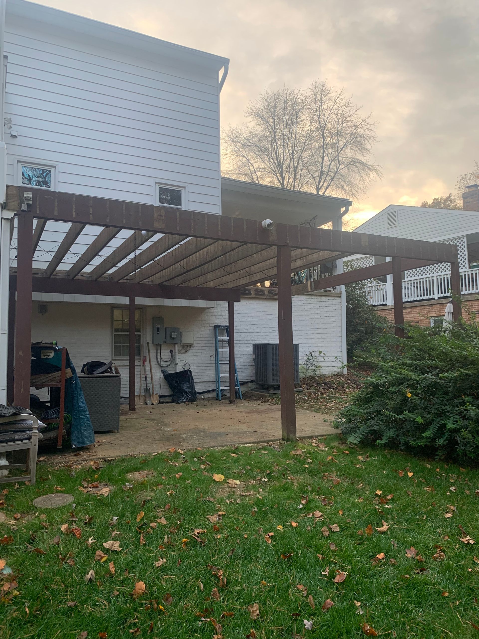 Backyard with pergola, house, and grassy lawn; overcast sky. Brown pergola has slatted roof.
