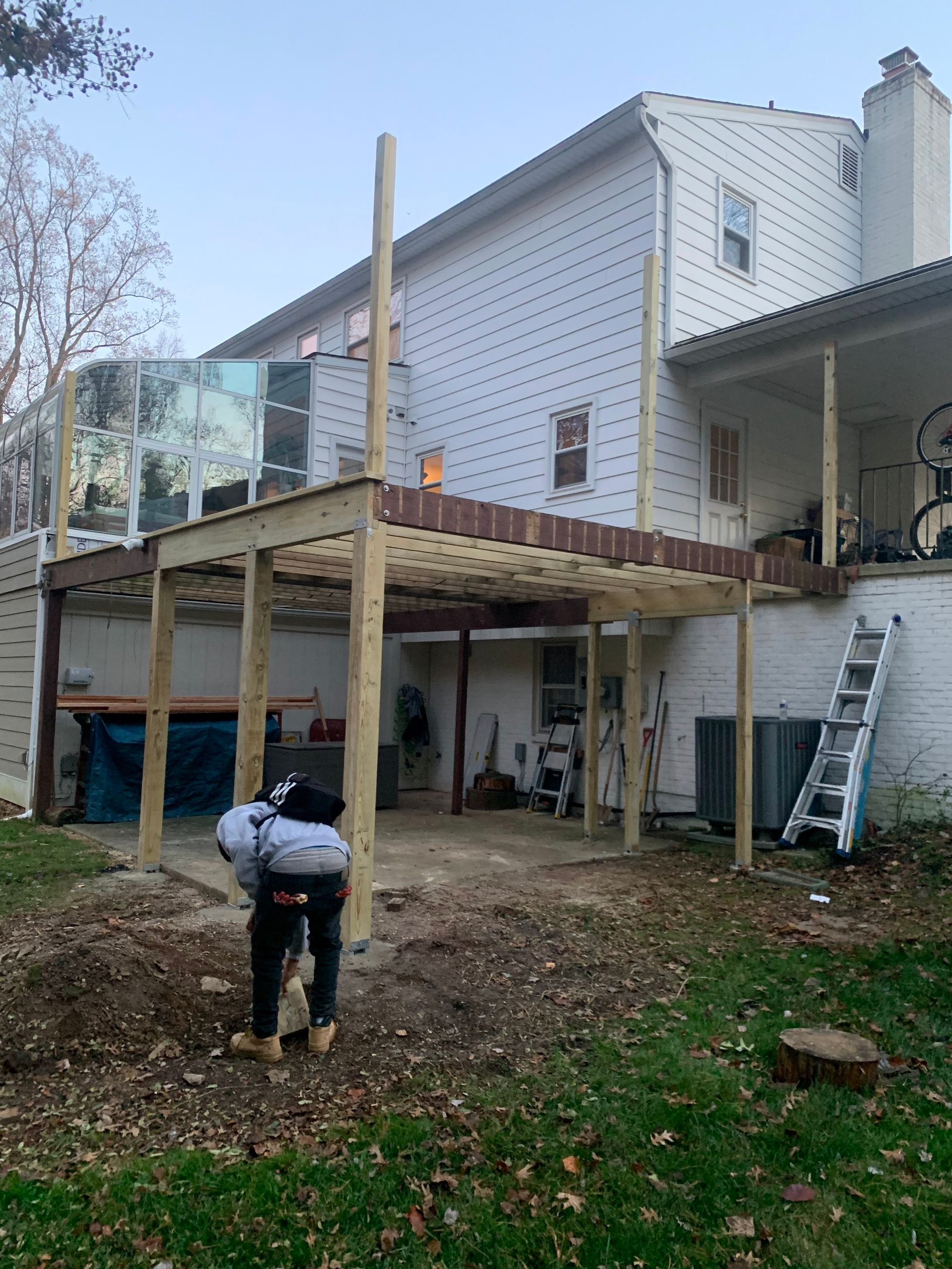 Person digging near a two-story deck under construction, attached to a white house.