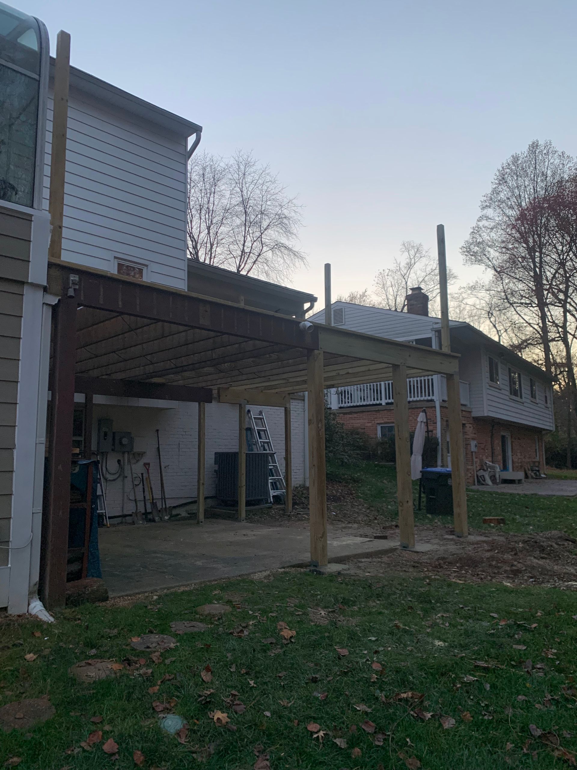 Newly constructed wooden deck attached to a house with supporting posts in a grassy yard, under an overcast sky.