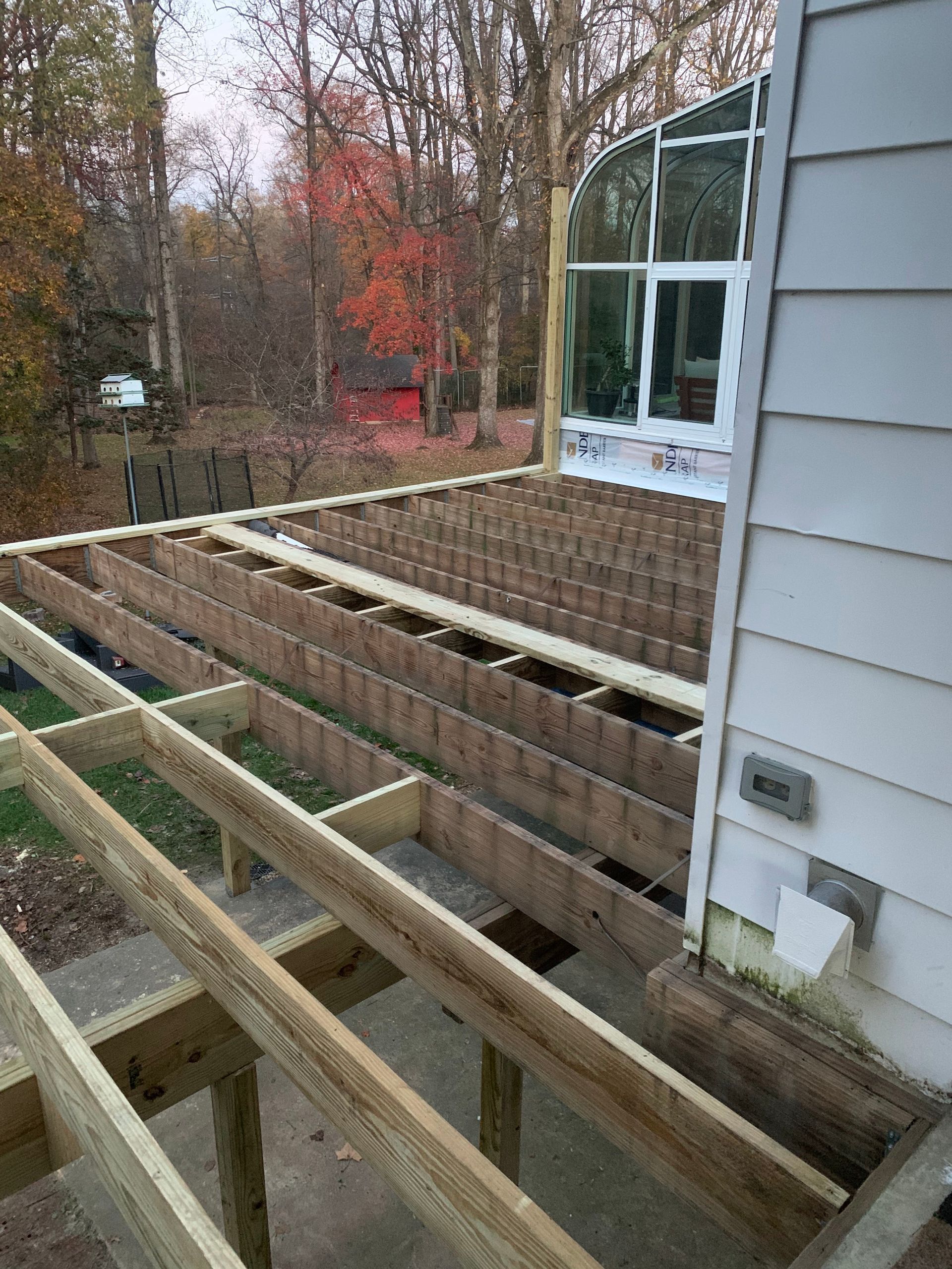 Partially built wooden deck with a house in the background and fall foliage.