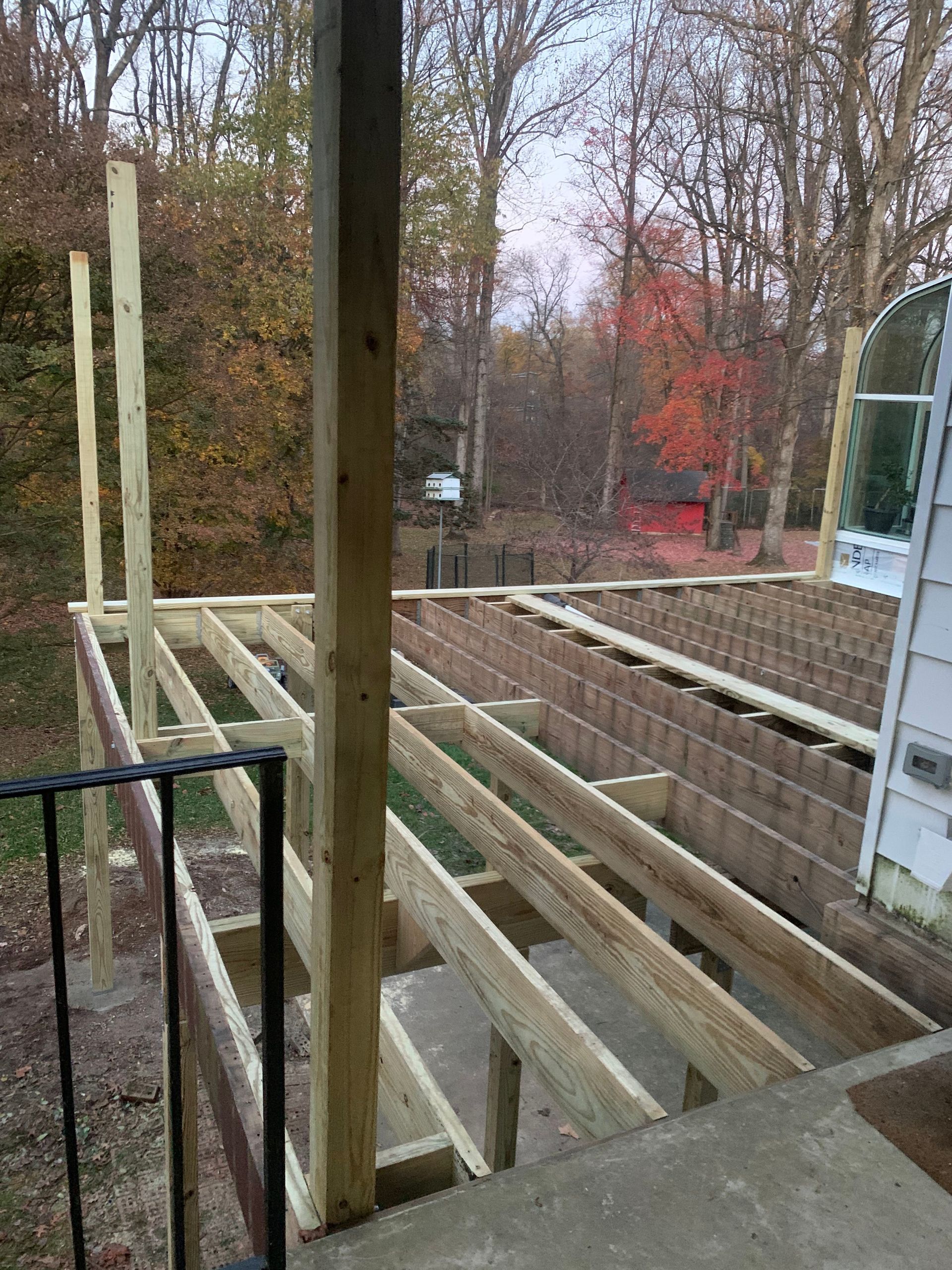Wooden deck under construction, with support beams and joists visible; outdoor setting.