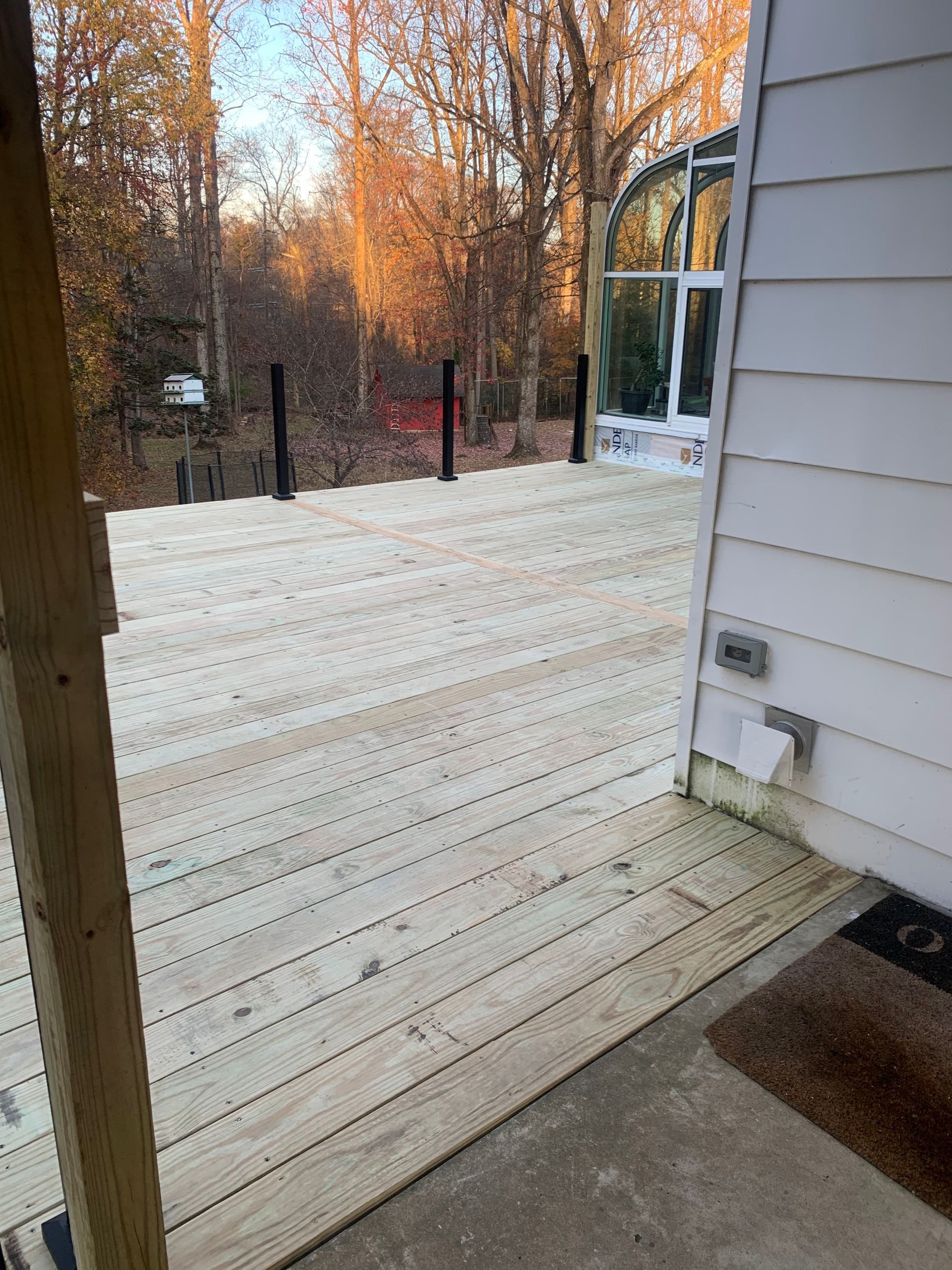 Wooden deck with black posts and glass-walled structure in the background, door on the right.