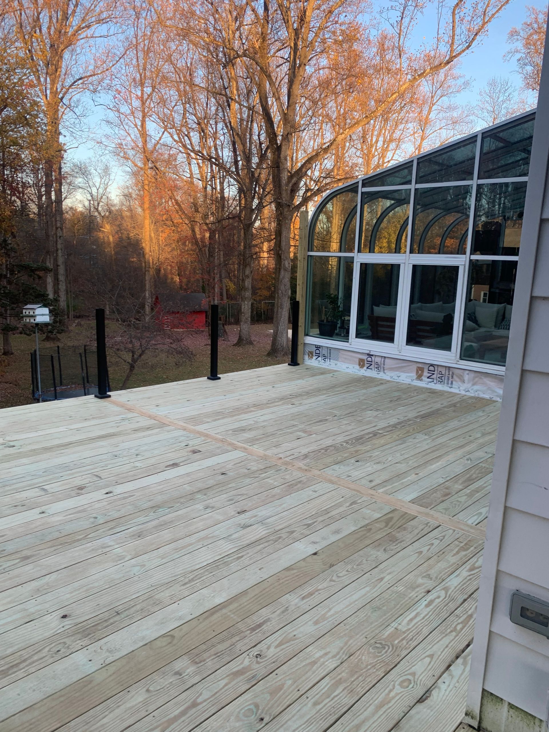 Wooden deck next to a glass-walled structure with a wooded background.