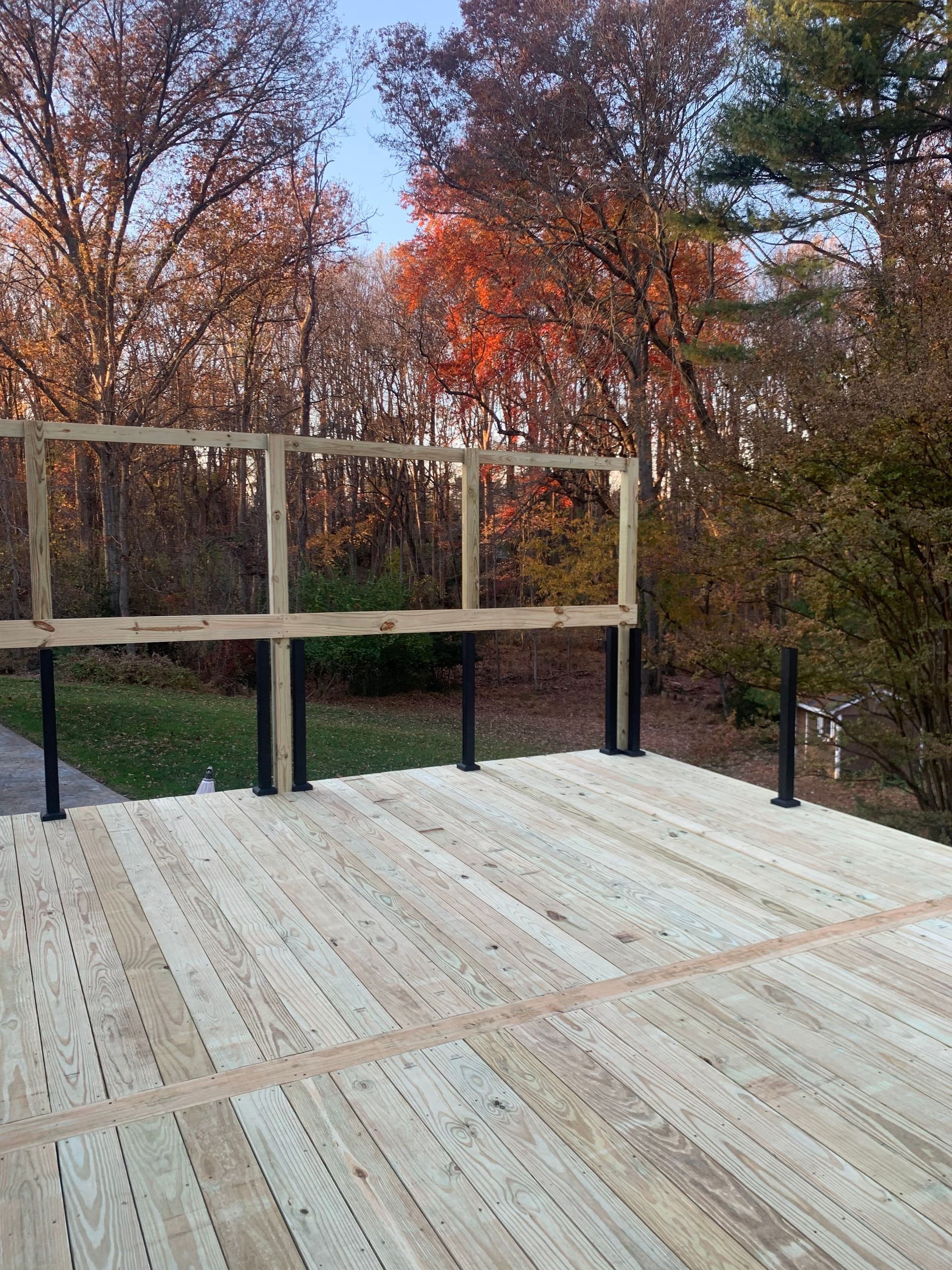 New wooden deck with incomplete railing against a backdrop of fall foliage.
