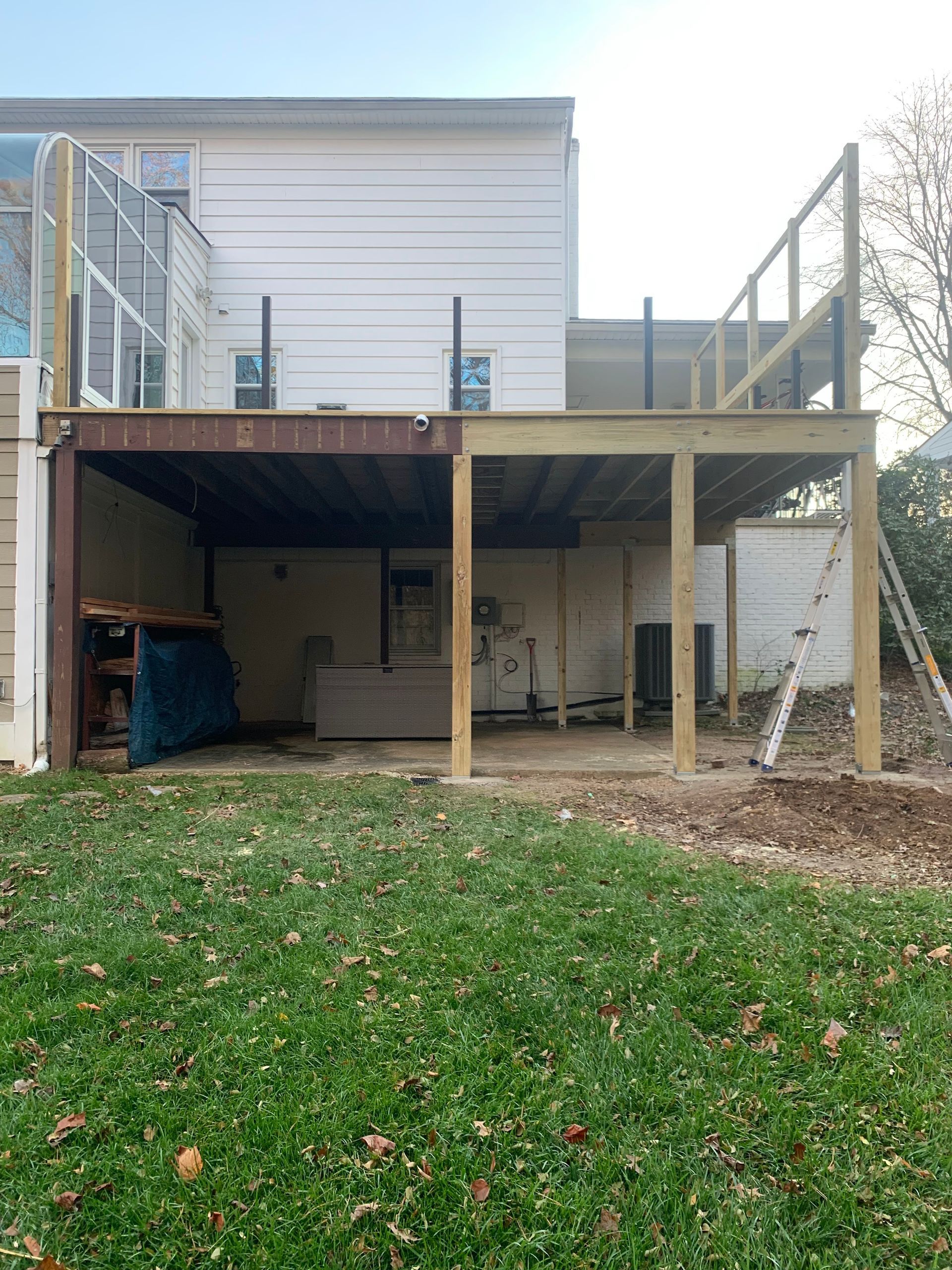 Backyard deck under construction; existing covered area has support beams, new deck frame partially built. Green lawn.