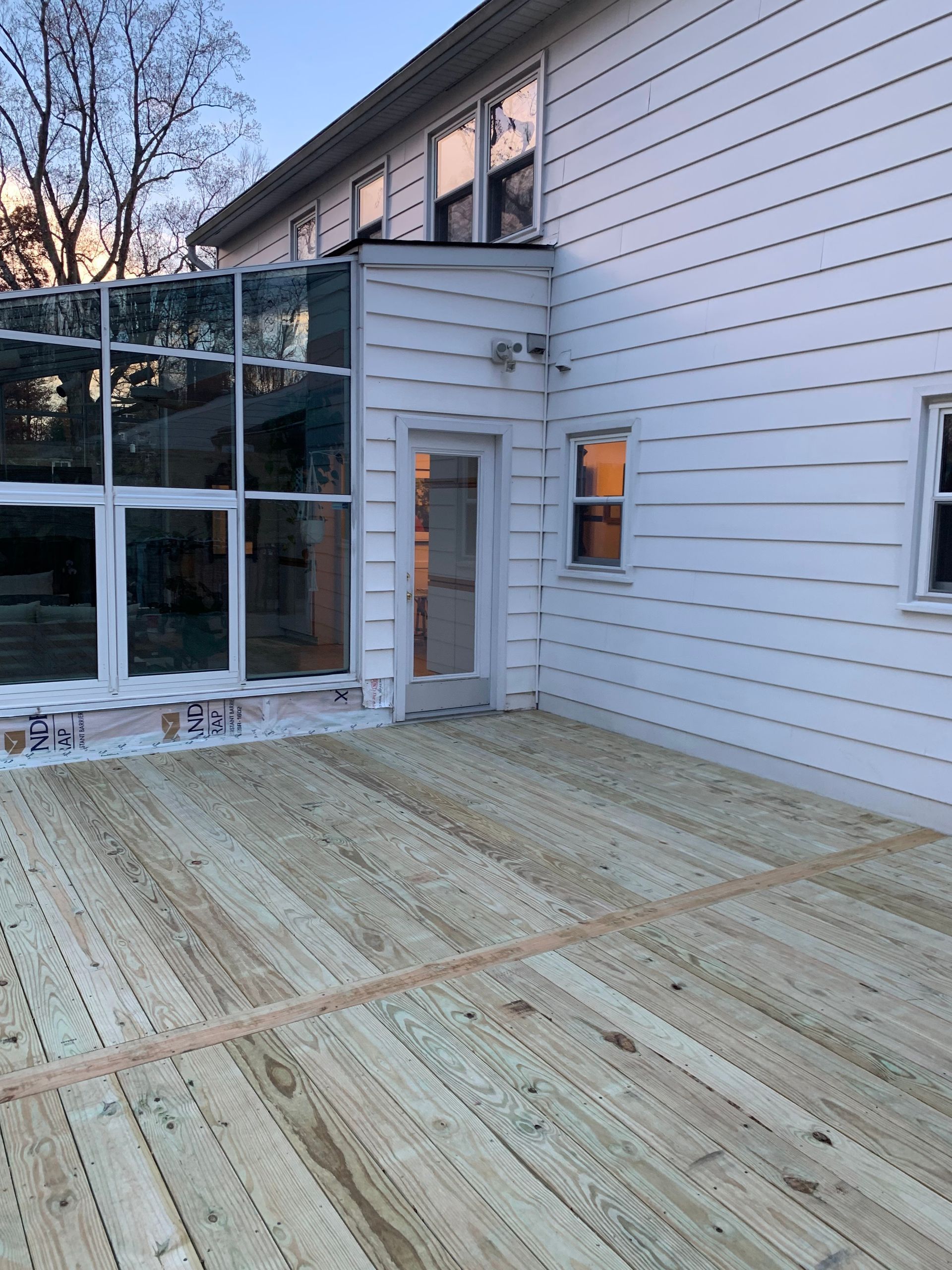 Exterior of a two-story white house with a new wooden deck, door, and glass-walled sunroom.