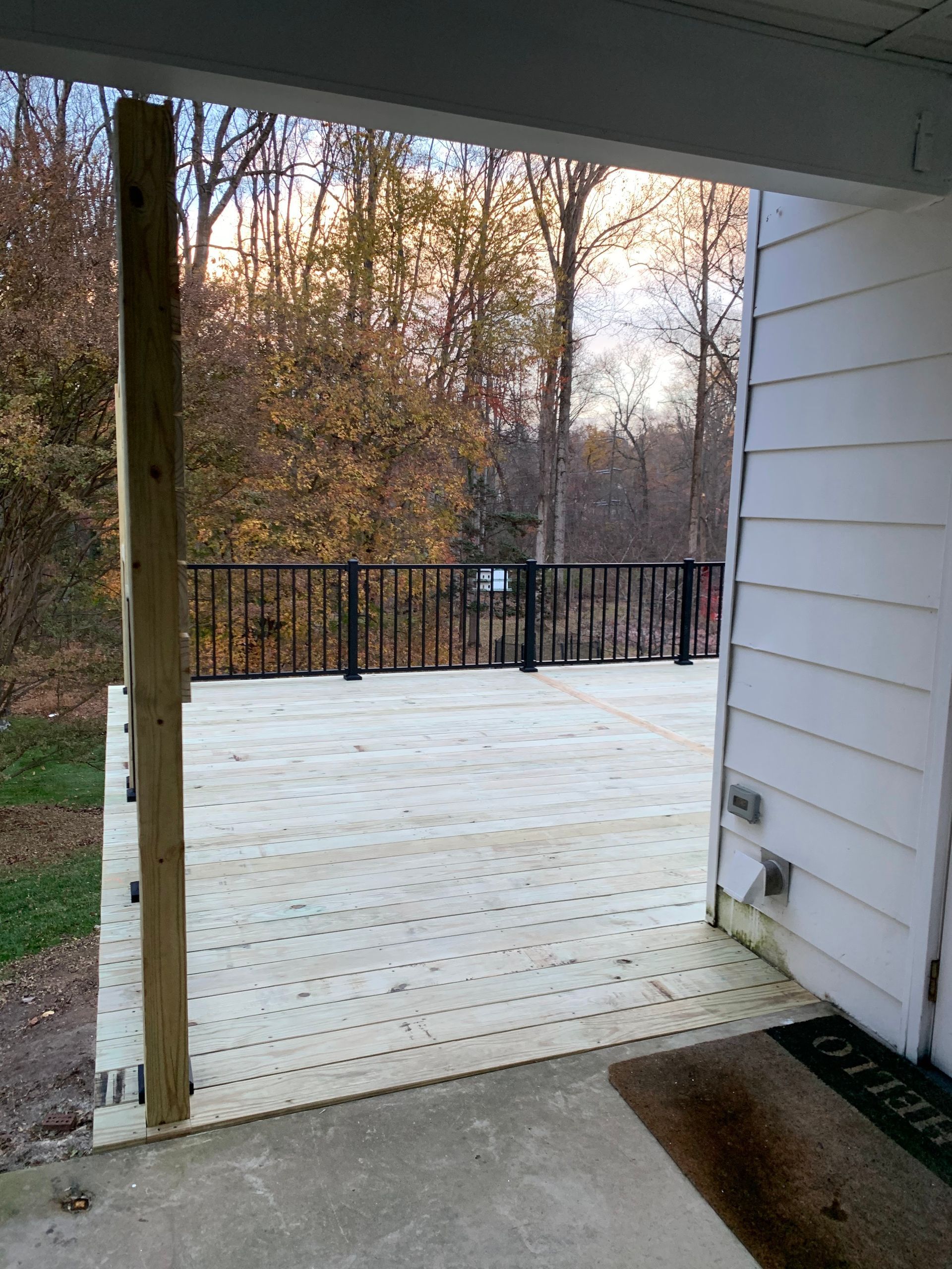 Wooden deck with black railing and surrounding trees. The deck is attached to a white-sided house.