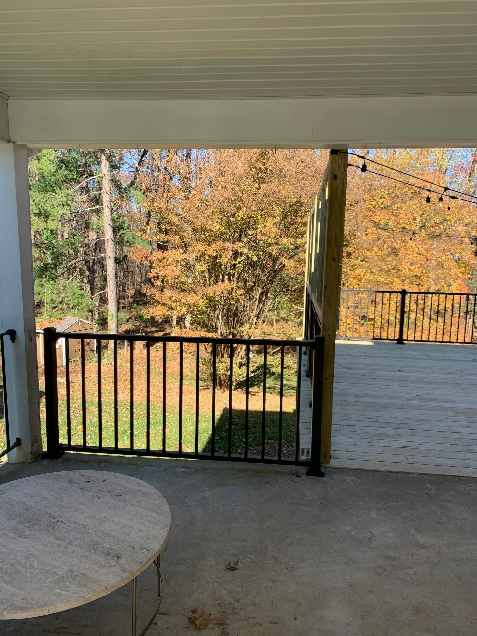 Covered patio overlooking autumn trees, featuring black railing and round table.