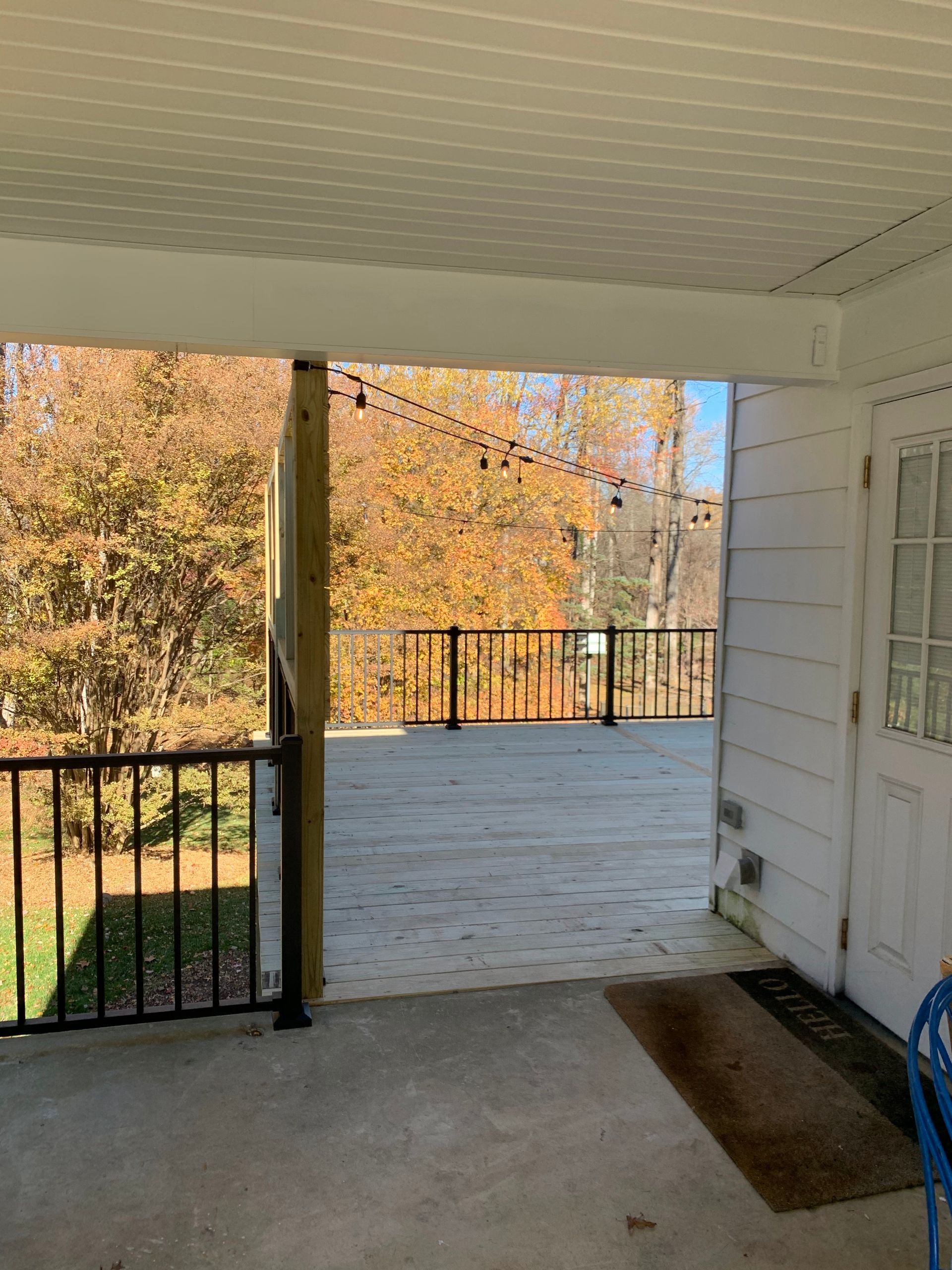 View of a deck and backyard from a covered porch, surrounded by fall foliage.